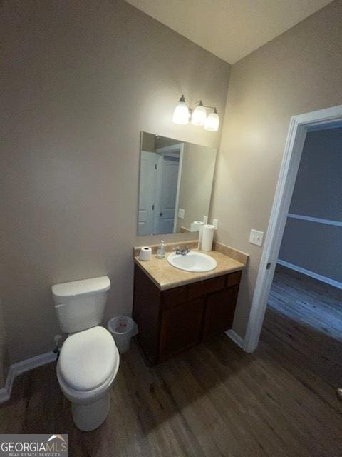 bathroom with toilet, wood finished floors, vanity, and baseboards