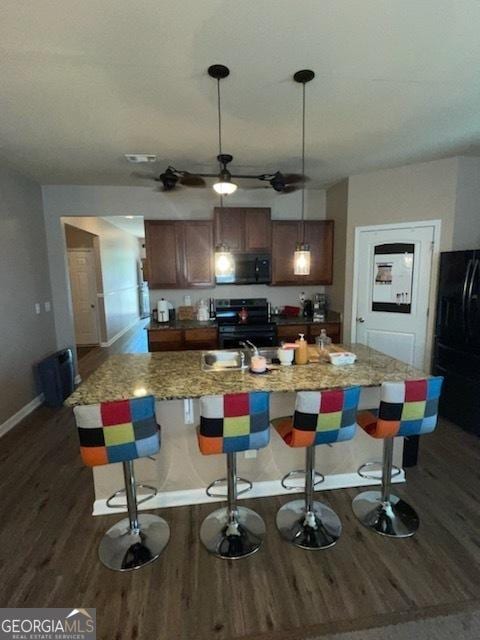 kitchen featuring stainless steel gas stove, baseboards, a kitchen breakfast bar, dark wood-style flooring, and freestanding refrigerator