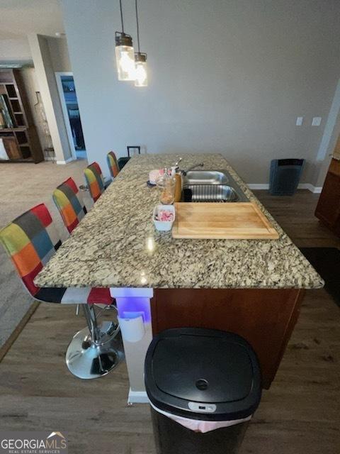 kitchen with wood finished floors, a sink, light stone counters, and baseboards