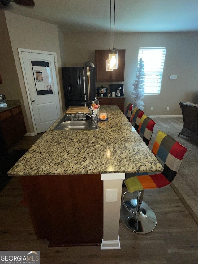 kitchen with baseboards, light stone counters, a center island, refrigerator, and a sink