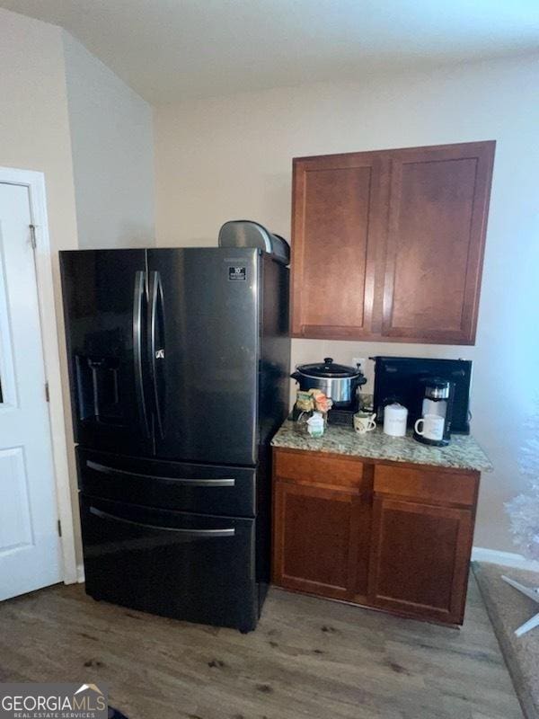 kitchen featuring brown cabinets, black fridge with ice dispenser, light wood-style flooring, and light stone countertops