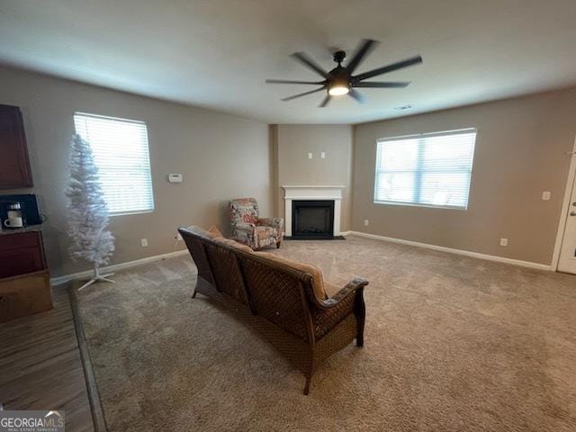 living room featuring a fireplace with flush hearth, baseboards, ceiling fan, and light colored carpet