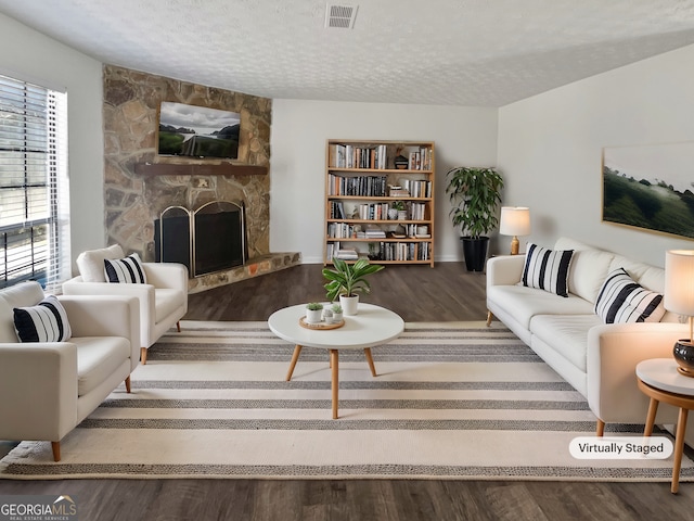 living room featuring a stone fireplace, visible vents, a textured ceiling, and wood finished floors