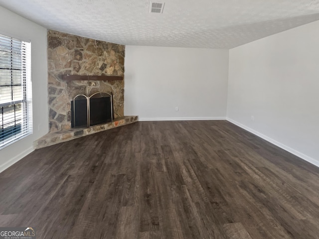 unfurnished living room with visible vents, dark wood finished floors, a textured ceiling, and a stone fireplace