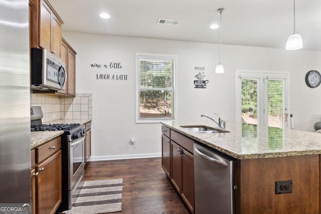 kitchen with dark wood-type flooring, a sink, appliances with stainless steel finishes, decorative backsplash, and light stone countertops