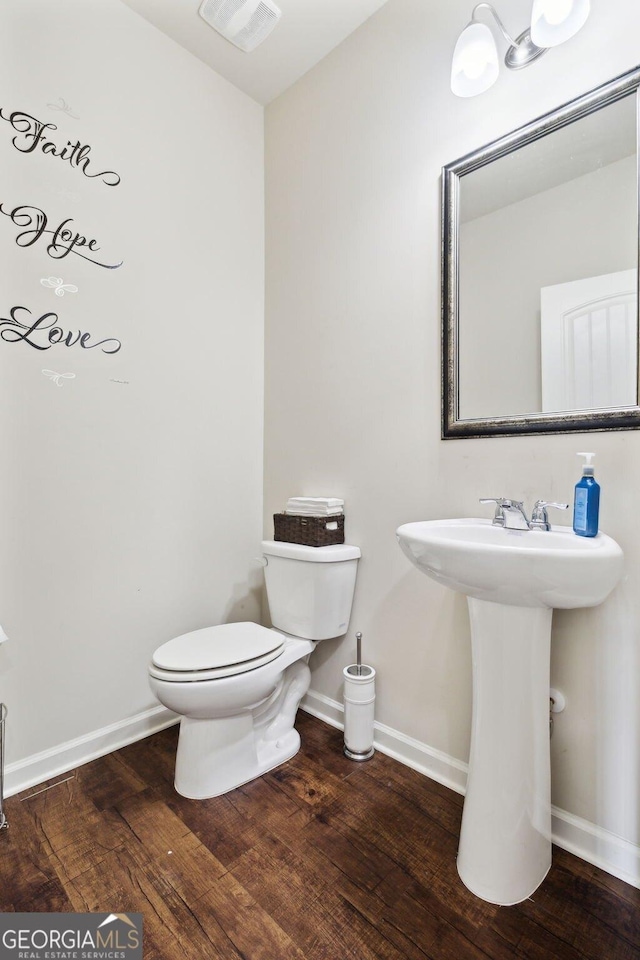 half bath with toilet, hardwood / wood-style flooring, baseboards, and visible vents