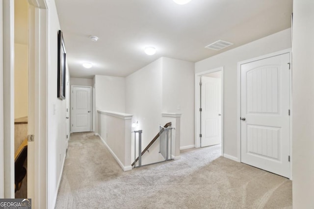 hallway with carpet, visible vents, baseboards, and an upstairs landing