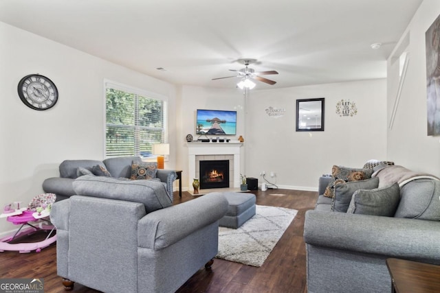 living room with dark wood-style floors, a tiled fireplace, a ceiling fan, and baseboards