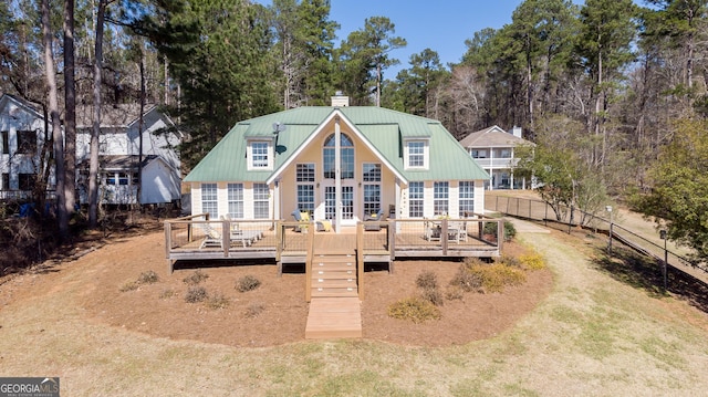 rear view of property featuring metal roof, a chimney, a wooden deck, and fence