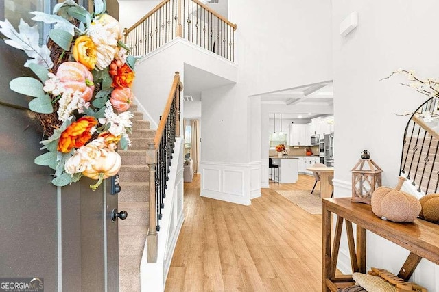 entryway featuring a wainscoted wall, a decorative wall, a high ceiling, light wood-type flooring, and stairs