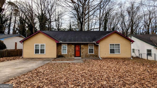 ranch-style house with driveway, stone siding, and fence