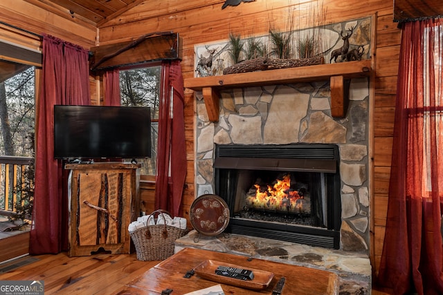 living area featuring visible vents, wood-type flooring, wooden walls, a stone fireplace, and vaulted ceiling