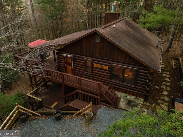 view of front of property featuring log siding, roof with shingles, and a chimney