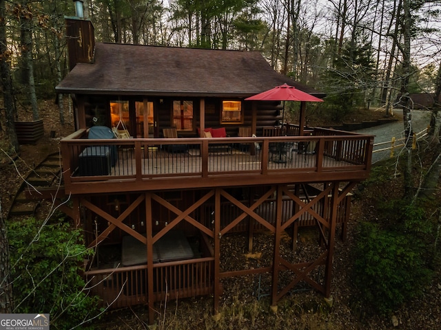 rear view of property with a deck, a chimney, and a shingled roof