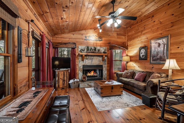 living area with hardwood / wood-style flooring, a stone fireplace, wood walls, lofted ceiling, and wood ceiling