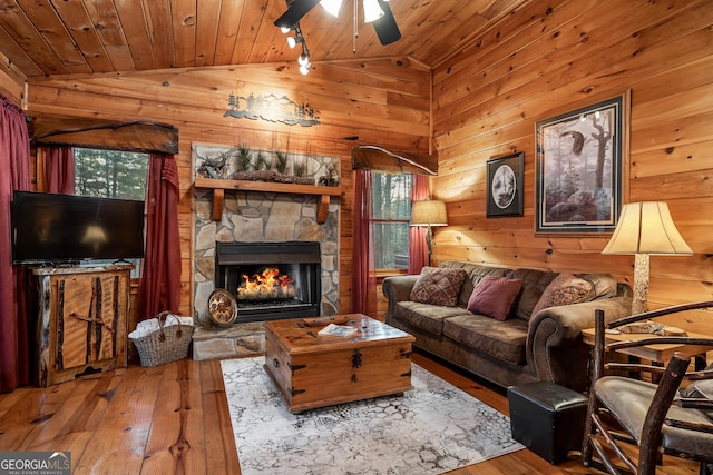 living room featuring hardwood / wood-style floors, wooden walls, lofted ceiling, a stone fireplace, and wood ceiling