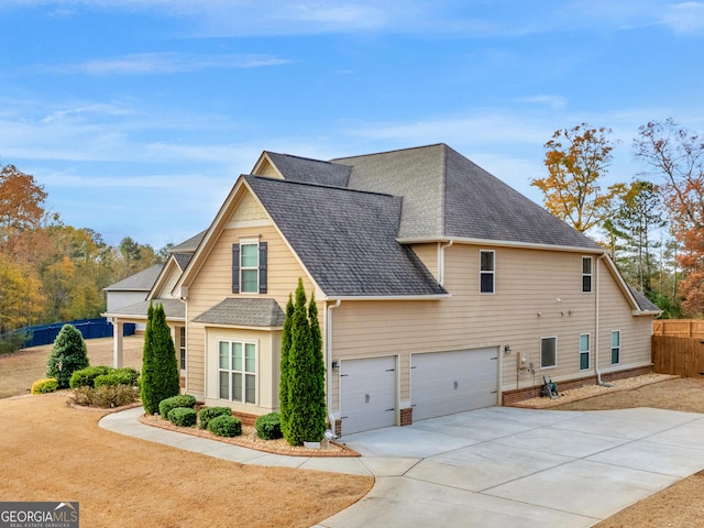 view of side of home featuring driveway, a shingled roof, an attached garage, and fence