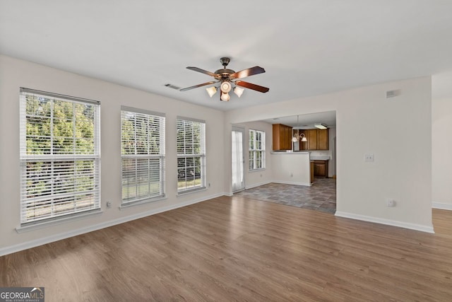 unfurnished living room with light wood-type flooring, visible vents, ceiling fan, and baseboards