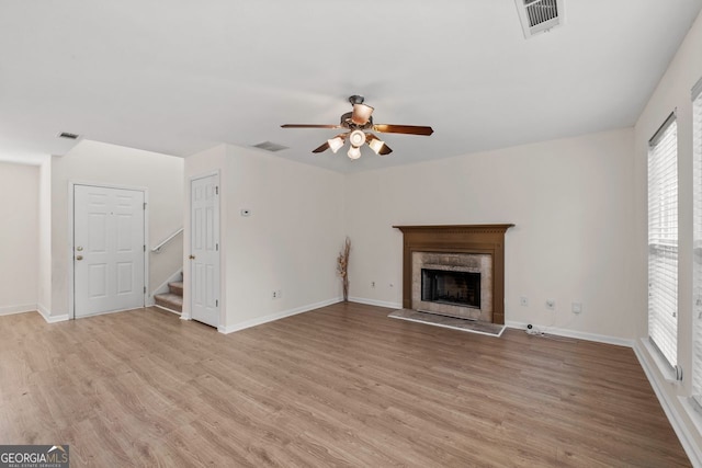 unfurnished living room featuring stairs, light wood-style flooring, a tile fireplace, and visible vents