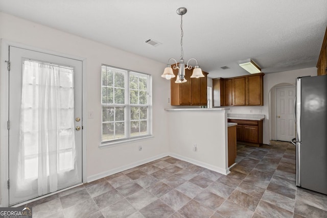 kitchen with brown cabinets, visible vents, hanging light fixtures, freestanding refrigerator, and a chandelier