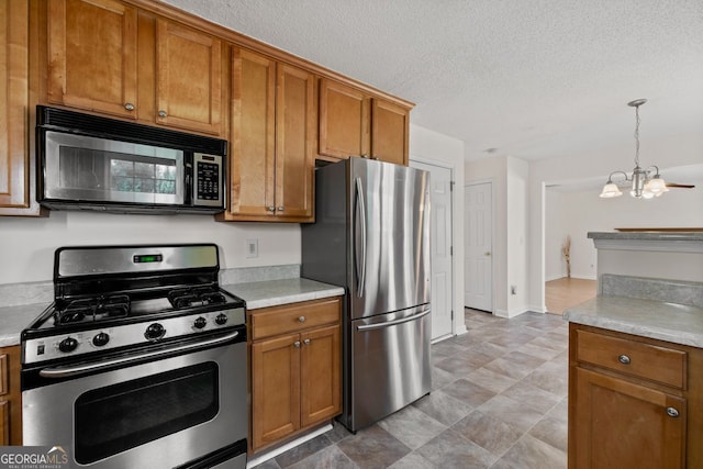 kitchen with pendant lighting, stainless steel appliances, light countertops, brown cabinetry, and a textured ceiling