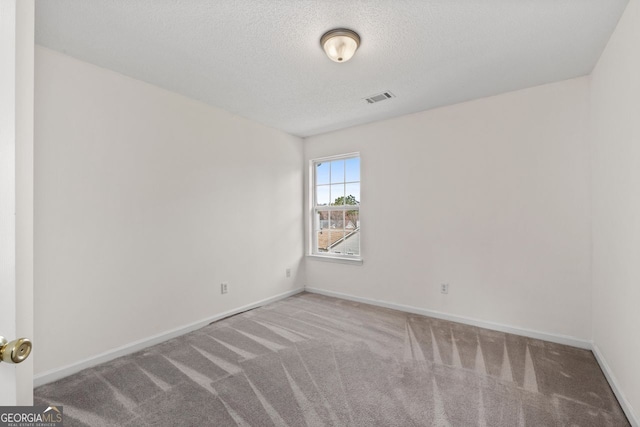 carpeted spare room featuring baseboards, visible vents, and a textured ceiling