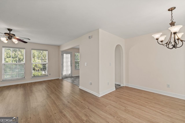 unfurnished living room featuring arched walkways, light wood finished floors, ceiling fan with notable chandelier, and baseboards