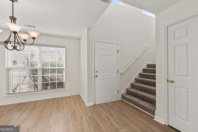 foyer entrance featuring baseboards, visible vents, stairway, wood finished floors, and a chandelier