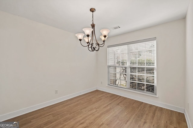 spare room with baseboards, visible vents, a chandelier, and wood finished floors