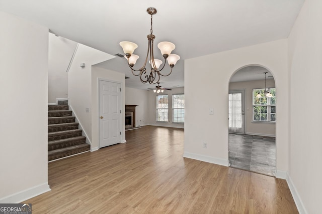 unfurnished dining area with arched walkways, light wood-type flooring, a fireplace, and plenty of natural light