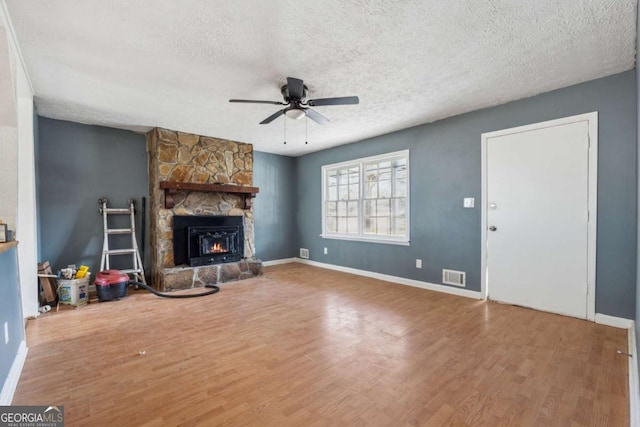 unfurnished living room with visible vents, a stone fireplace, a textured ceiling, and wood finished floors