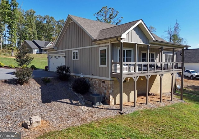 view of front facade with driveway, a shingled roof, an attached garage, cooling unit, and board and batten siding