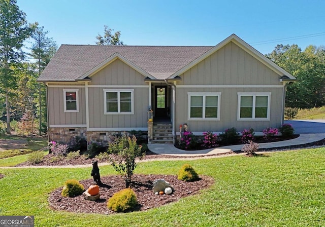 view of front of property with stone siding, a shingled roof, board and batten siding, and a front yard