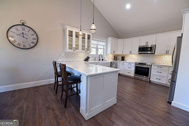 kitchen with white cabinets, glass insert cabinets, appliances with stainless steel finishes, a breakfast bar area, and a peninsula