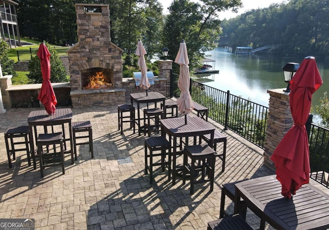 view of patio with a water view, an outdoor stone fireplace, and a boat dock