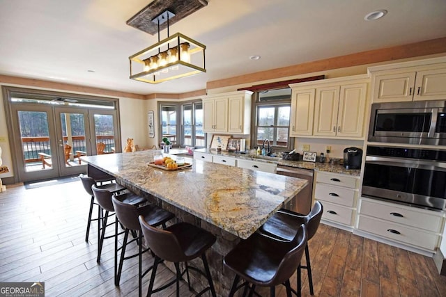 kitchen with cream cabinets, a breakfast bar area, french doors, appliances with stainless steel finishes, and dark wood-style floors