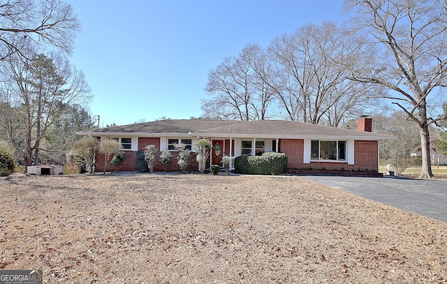 ranch-style house featuring driveway, brick siding, and a chimney