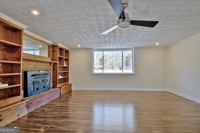 unfurnished living room with a textured ceiling, wood finished floors, baseboards, a wood stove, and crown molding