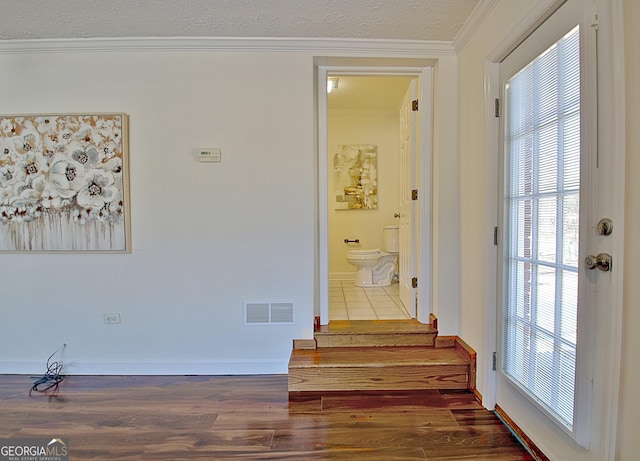 corridor featuring a textured ceiling, wood finished floors, visible vents, baseboards, and crown molding