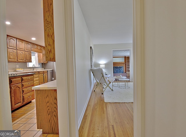 kitchen with baseboards, a glass covered fireplace, brown cabinets, light countertops, and a sink