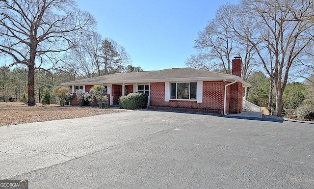 single story home with aphalt driveway, brick siding, and a chimney