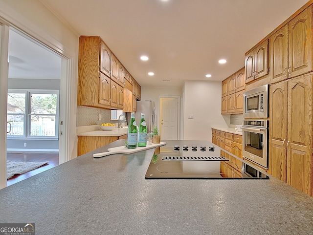 kitchen with recessed lighting, backsplash, appliances with stainless steel finishes, a sink, and baseboards