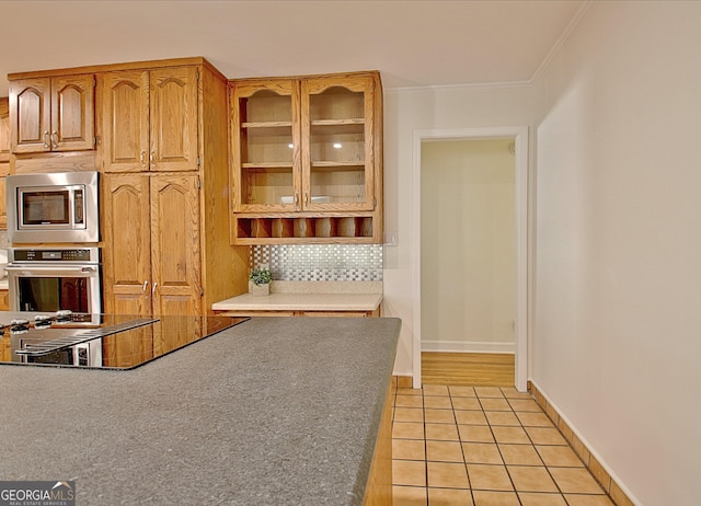 kitchen with light tile patterned floors, baseboards, appliances with stainless steel finishes, glass insert cabinets, and crown molding