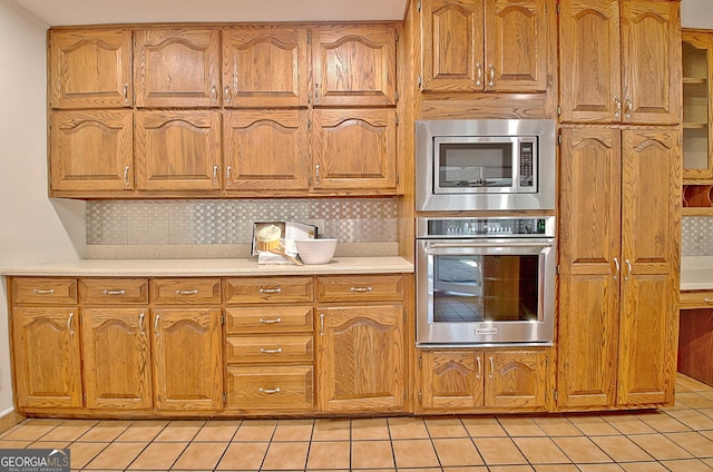 kitchen with light tile patterned floors, stainless steel appliances, light countertops, decorative backsplash, and brown cabinetry