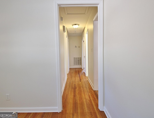 hall featuring baseboards, attic access, visible vents, and wood finished floors