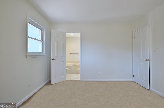 unfurnished bedroom featuring connected bathroom, baseboards, and carpet flooring