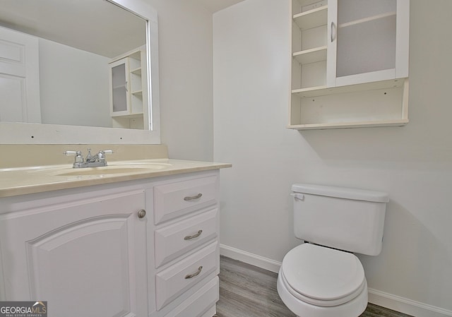 half bathroom with vanity, wood finished floors, toilet, and baseboards