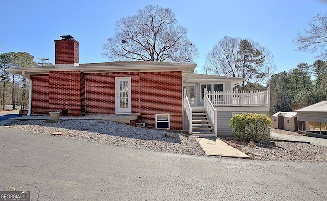 view of front of house featuring an outbuilding, brick siding, a chimney, and a storage unit