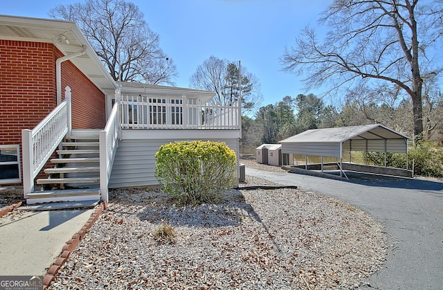 view of side of property featuring brick siding, stairway, central AC unit, a carport, and driveway