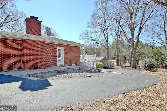 exterior space with brick siding, a chimney, and stairs